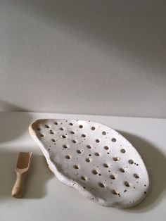 a white ceramic object with holes on the surface next to a small wooden spatula