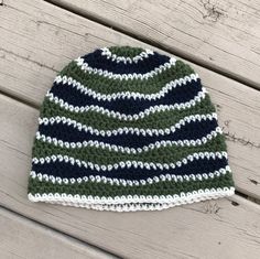 a green and white knitted hat sitting on top of a wooden table next to a pair of scissors