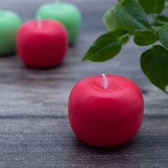 three red and green candles sitting on top of a table next to a potted plant