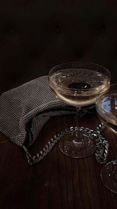 two wine glasses sitting on top of a wooden table next to a cloth covered bag