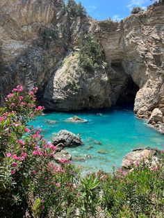 the blue water is surrounded by large rocks and pink flowers on the side of it