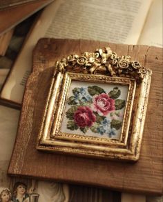 a cross stitch picture frame sitting on top of an old book with flowers in it