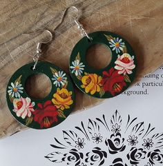 a pair of wooden earrings with flowers painted on them sitting next to a piece of paper