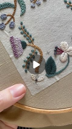 someone is stitching on a piece of fabric with flowers and leaves in the middle