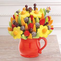 a red mug filled with assorted fruit and chocolate candies on top of a wooden table