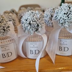 three small bottles with flowers in them on a wooden table next to some white ribbons