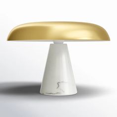 a white and gold table lamp on a white surface with an oval light fixture in the middle