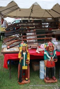 two figurines sitting on top of a red table under a tent with other items