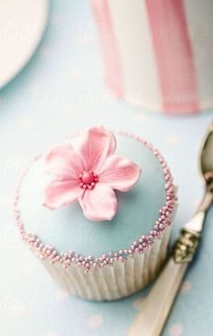 a pink flower on top of a cupcake next to a silver spoon and fork