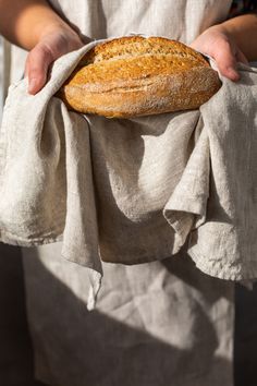 a person holding a loaf of bread on top of a white cloth in their hands