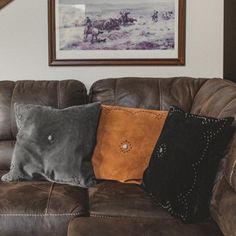 a couch with two pillows on it in front of a framed painting and a brown chair