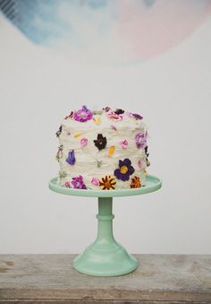 a cake with white frosting and multicolored flowers sitting on a green plate