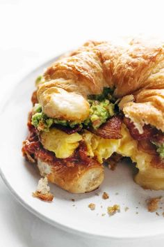 a croissant sandwich with bacon and avocado is on a white plate