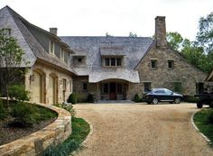 a black car parked in front of a large stone house with a driveway leading to it