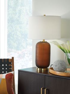 a lamp on top of a dresser next to a vase with flowers and rocks in it