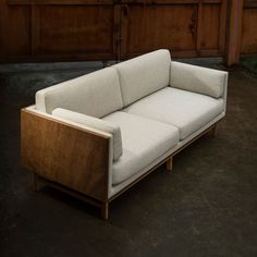 a white couch sitting on top of a cement floor next to a wooden fence and wall