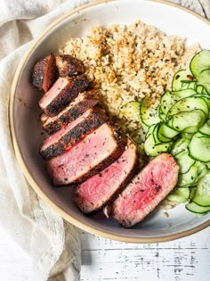 a white bowl filled with meat, rice and cucumbers