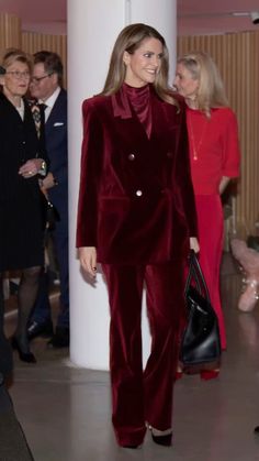 a woman in a red velvet suit walking down a hall with other people behind her