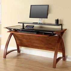 a wooden desk with a computer monitor and keyboard on it, in front of a beige wall