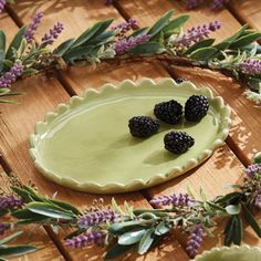 three blackberries are placed on a pie plate surrounded by greenery and lavenders