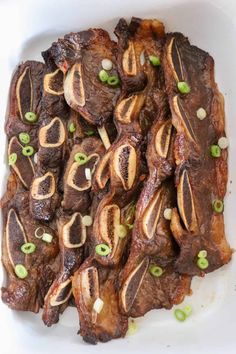 a white plate topped with ribs covered in sauce and green onions