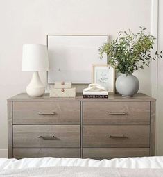 a dresser with two vases on top of it next to a mirror and lamp