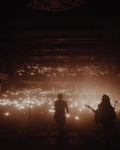 two people standing in front of a stage with lots of lights on the walls and floor