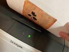 a hand is holding a roll of paper over a printer