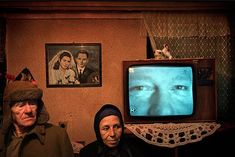 two people sitting in front of a tv with an old woman looking at the screen