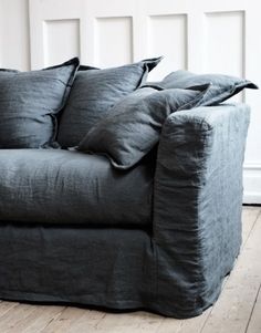 a couch with pillows on it sitting in front of a white paneled wall and wooden floor