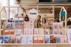 a man and woman standing behind a table full of greeting cards at a book store