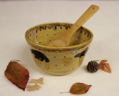 a wooden spoon sitting in a bowl next to some leaves and a pine cone on the table