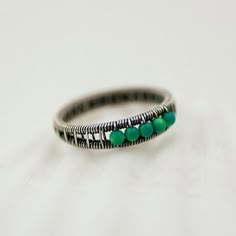 a close up of a ring on a white surface with green beads and black wire