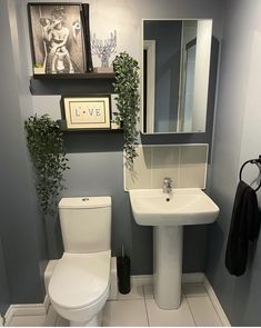 a white toilet sitting next to a sink in a bathroom under pictures on the wall