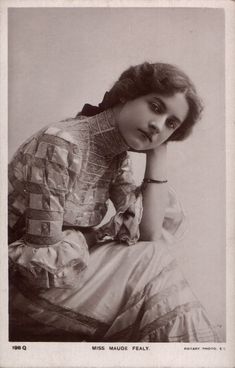 an old black and white photo of a woman in dress sitting on the ground with her hand under her chin