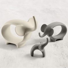 three elephant shaped objects sitting next to each other on a white surface and one is grey