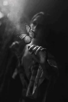 a woman holding a butterfly in her hand and looking at it with the light shining on her face