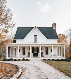 a white house with black shingles and porches on the front door is surrounded by autumn foliage