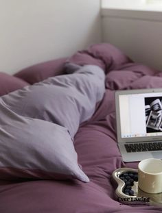 an open laptop computer sitting on top of a bed next to a cup of coffee