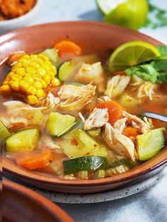 a bowl filled with chicken and vegetable soup next to a plate of corn on the cob