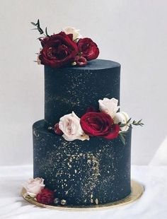 a three tiered black cake with red and white flowers on it's side