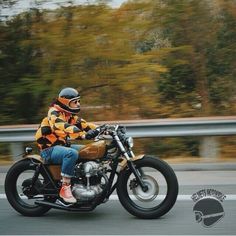 a man riding on the back of a motorcycle down a road in front of trees