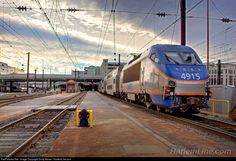 a blue and silver train traveling down tracks next to a station with power lines above it