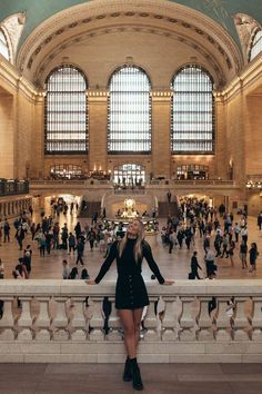 a woman standing in the middle of a train station with lots of people walking around