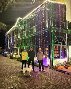 two men and a dog standing in front of a building with christmas lights on it