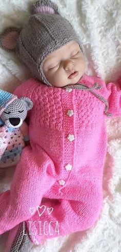 a baby sleeping next to a stuffed animal on top of a white blanket and wearing a knitted hat