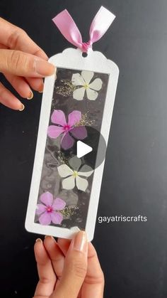 someone is holding up an ornament with pink and white flowers on it in front of a black background