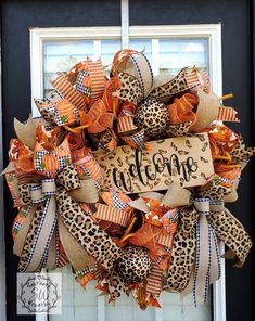 a leopard print wreath with the word welcome on it and an animal print bow hanging from the front door