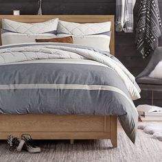 a bed with grey and white comforter next to a pair of shoes on the floor