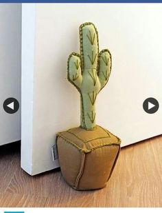 a small stuffed cactus sitting on top of a wooden floor next to a white wall